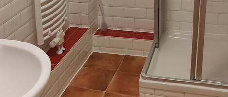 A bathroom with white and red-tiled walls, a white sink, and a glass shower enclosure.
