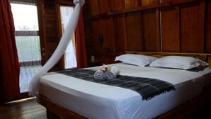 Een houten bed met witte lakens, een opgerolde handdoek en een decoratief kussen.
