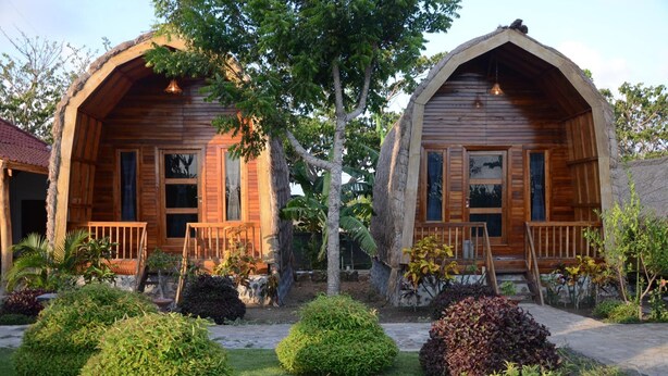 Twee houten vakantiehuisjes met balkons, omringd door verzorgde tuinen en bomen.