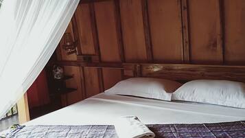 Una cama con sábanas blancas, una toalla enrollada y una alfombra estampada.