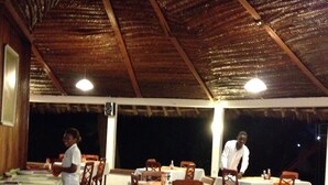 An outdoor dining area with tables and chairs, a thatched roof, and a view of the night sky. - Panori Hotel (Tanga)