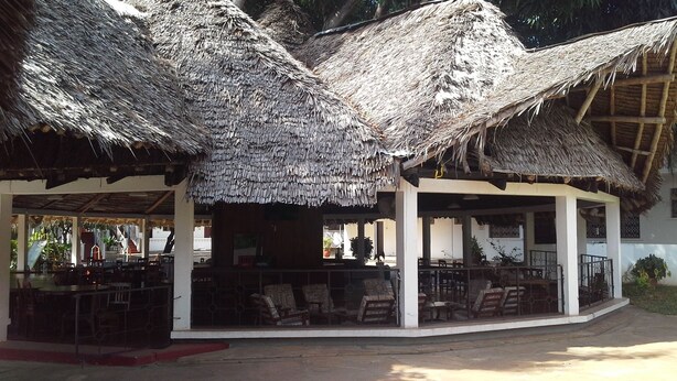 A covered outdoor seating area with thatched roofs and wooden furniture. - Panori Hotel (Tanga)