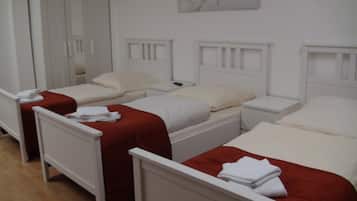 A hotel room with three single beds, each with a white headboard and a red blanket. There is a white nightstand with a remote control on it.