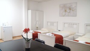 A hotel room with two beds, a small refrigerator, a vase with a flower, and a painting on the wall. - Apartment Osterstraße 322 zwei (Hannover)