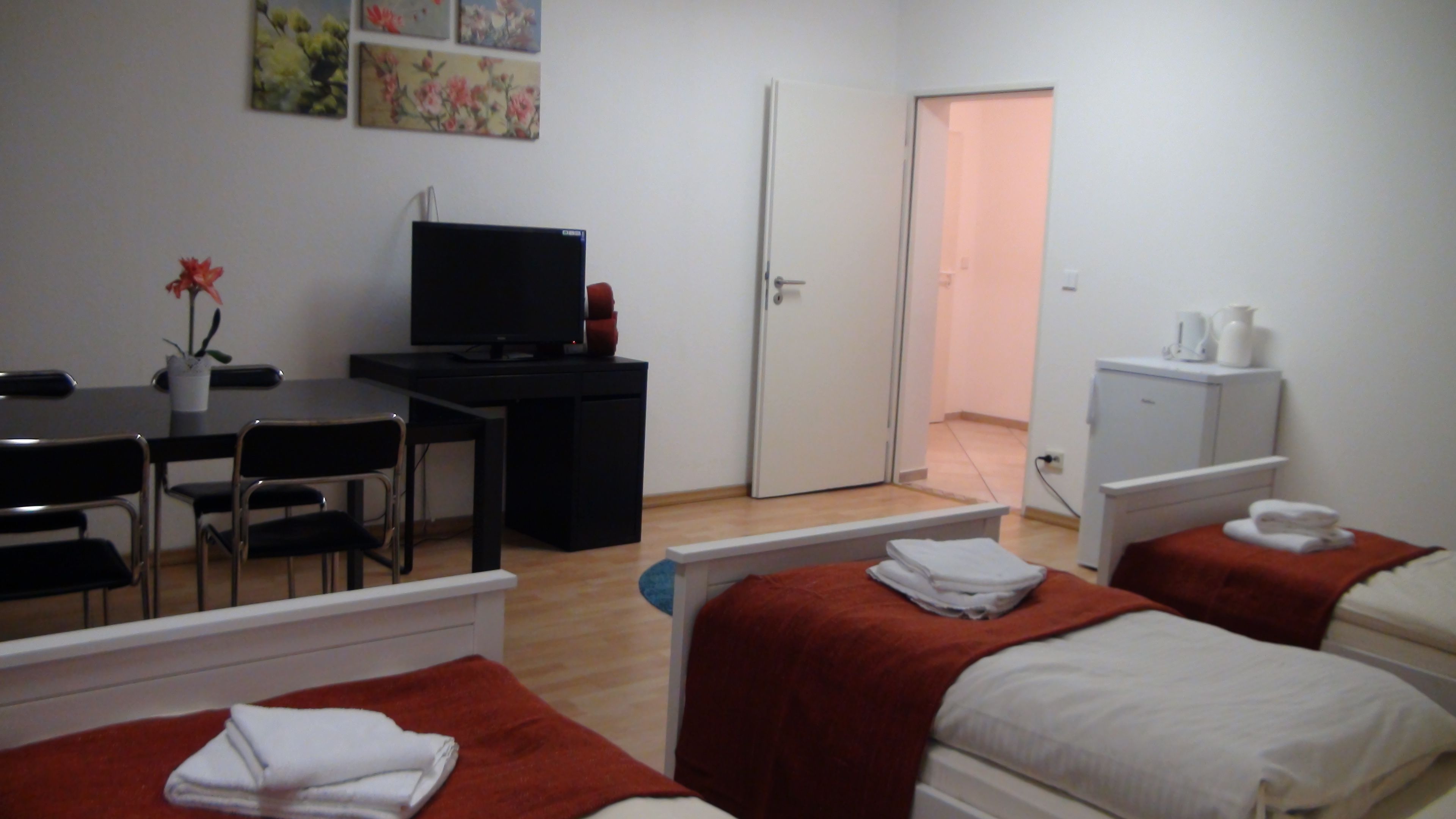 Una habitación de hotel con dos camas, un escritorio con silla, televisor, una puerta y un mueble pequeño.