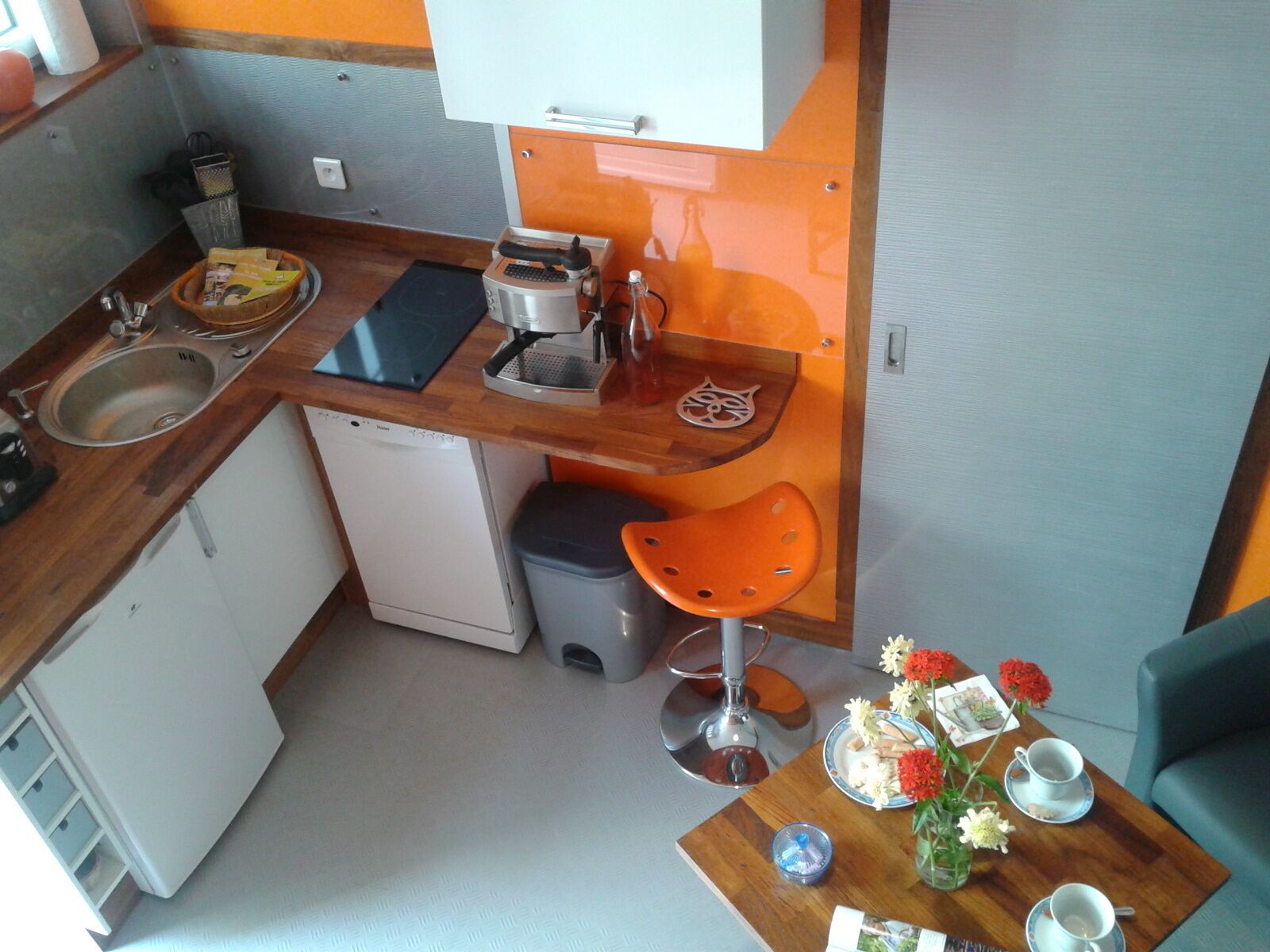 A compact kitchenette with a sink, coffee maker, and orange bar stool.