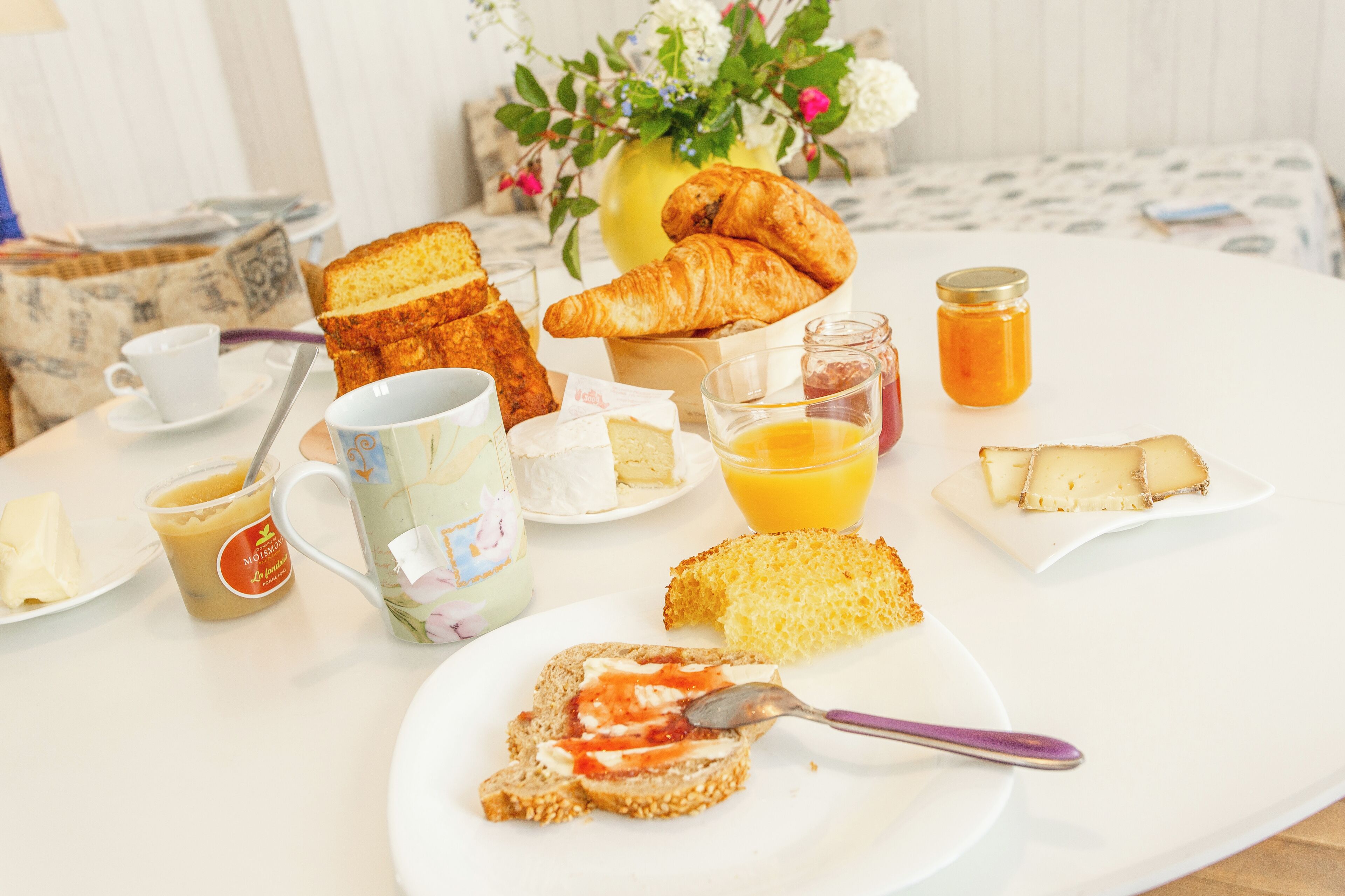 A breakfast table with croissants, toast, jam, butter, and a mug of coffee.