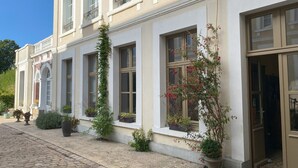 Ein Gebäude mit mehreren Fenstern, einige mit Pflanzen, einem Kopfsteinpflasterweg und einer Tür.