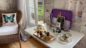 Ein gemütliches Zimmer mit einem Korbstuhl, einem Tisch mit einer Weinflasche, Gläsern und kleinen Schalen mit Speisen.