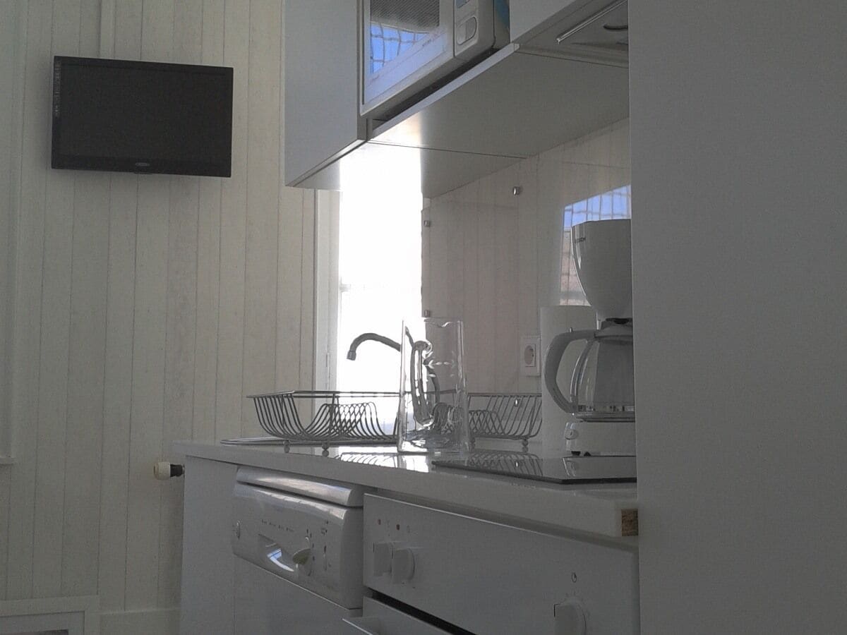 A kitchen with white cabinets, a microwave, a coffee maker, and a sink with a metal basket.