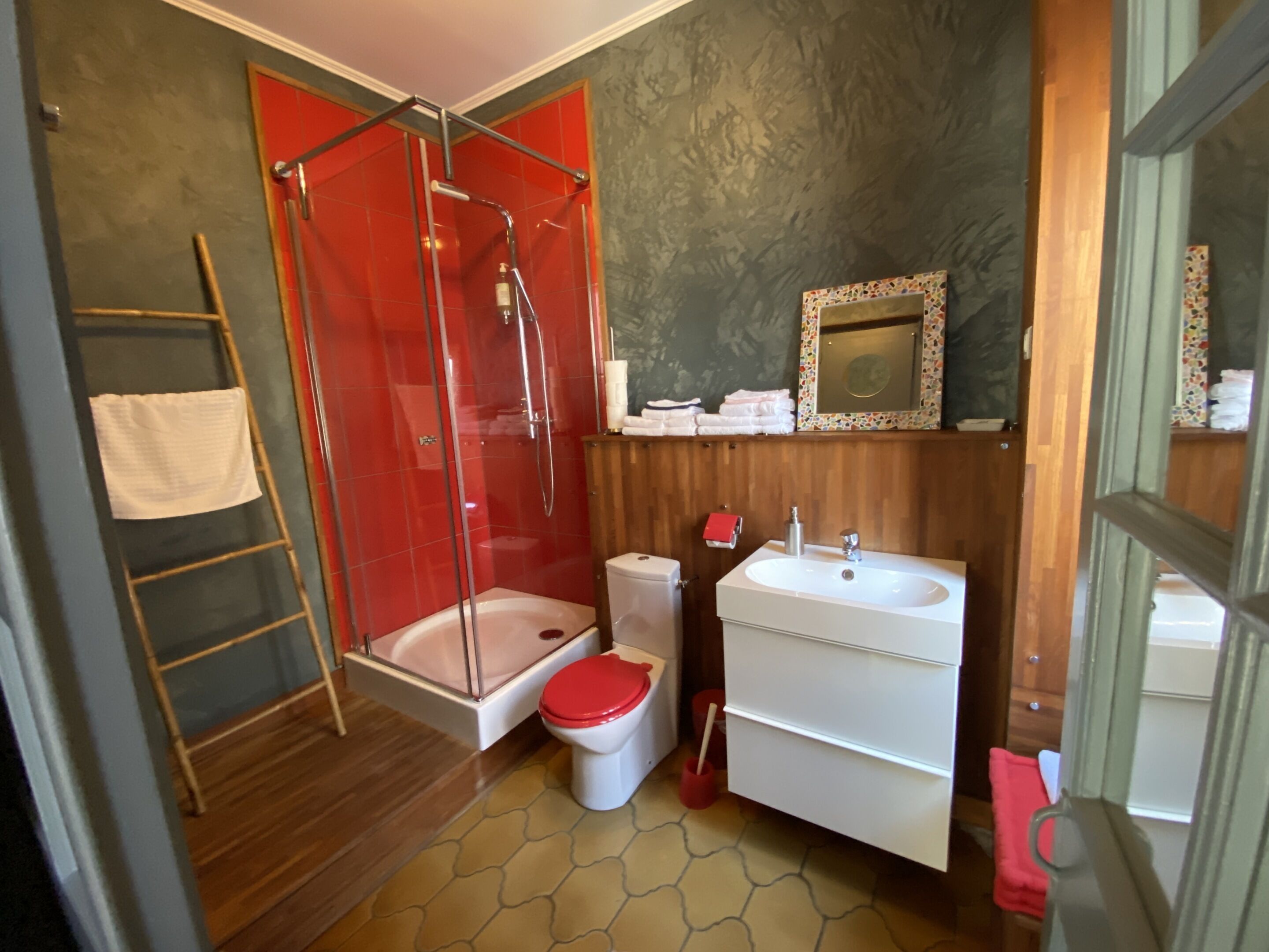A bathroom with a glass shower enclosure, a toilet, a sink, and a mirror.