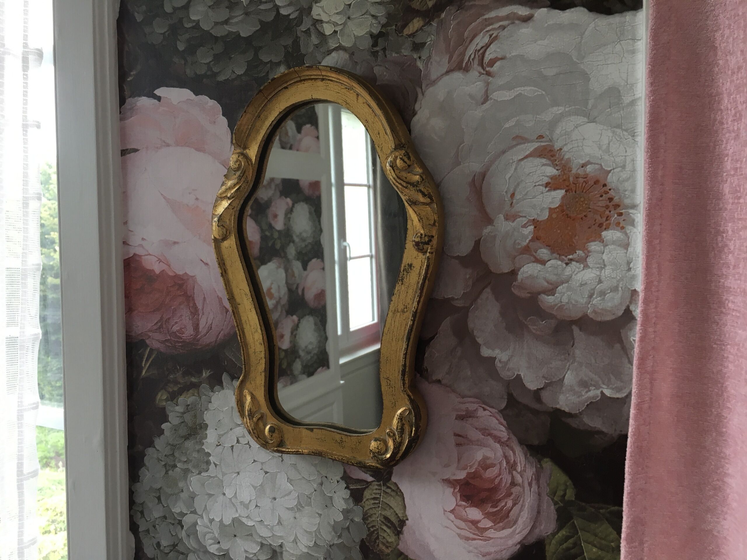 A mirror with an ornate frame against a floral wallpaper backdrop.