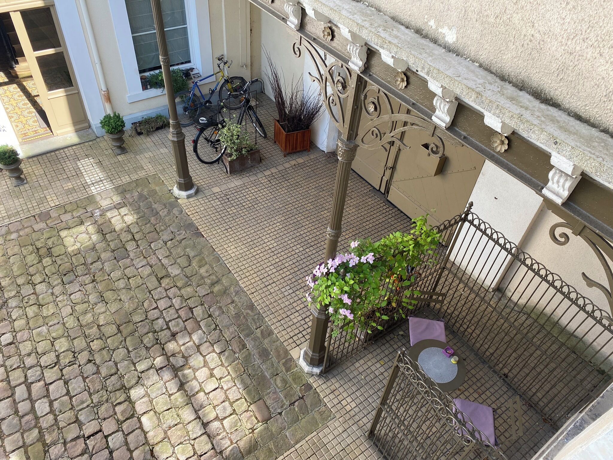 A courtyard with cobblestone flooring, a metal fence, potted plants, and bicycles.