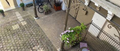 A courtyard with cobblestone flooring, a metal fence, potted plants, and bicycles.