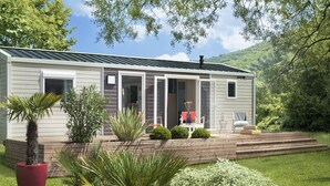 A single-story cabin with a covered porch, a small deck, and a landscaped garden with various plants.