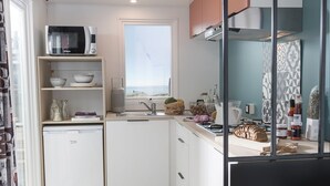 A compact kitchen with white cabinets, a microwave, a small refrigerator, and a window providing natural light.