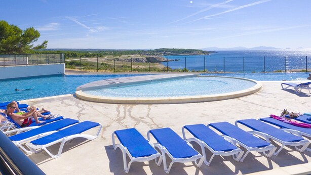 A pool area with blue lounge chairs and a view of the sea.