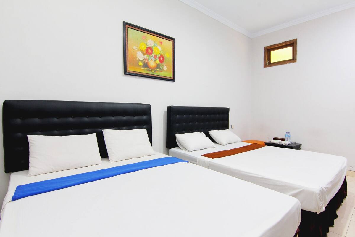 Two single beds with black headboards, white bedding, and a blue runner. A painting hangs on the wall above the beds.