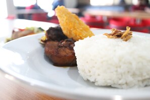 A plate with white rice, a piece of meat, and fried food. - Hotel Popi Pondok Pisang (Ngaglik)