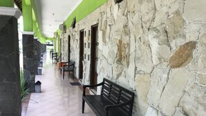 A corridor with stone walls, benches, and trash bins. - Hotel Popi Pondok Pisang (Ngaglik)