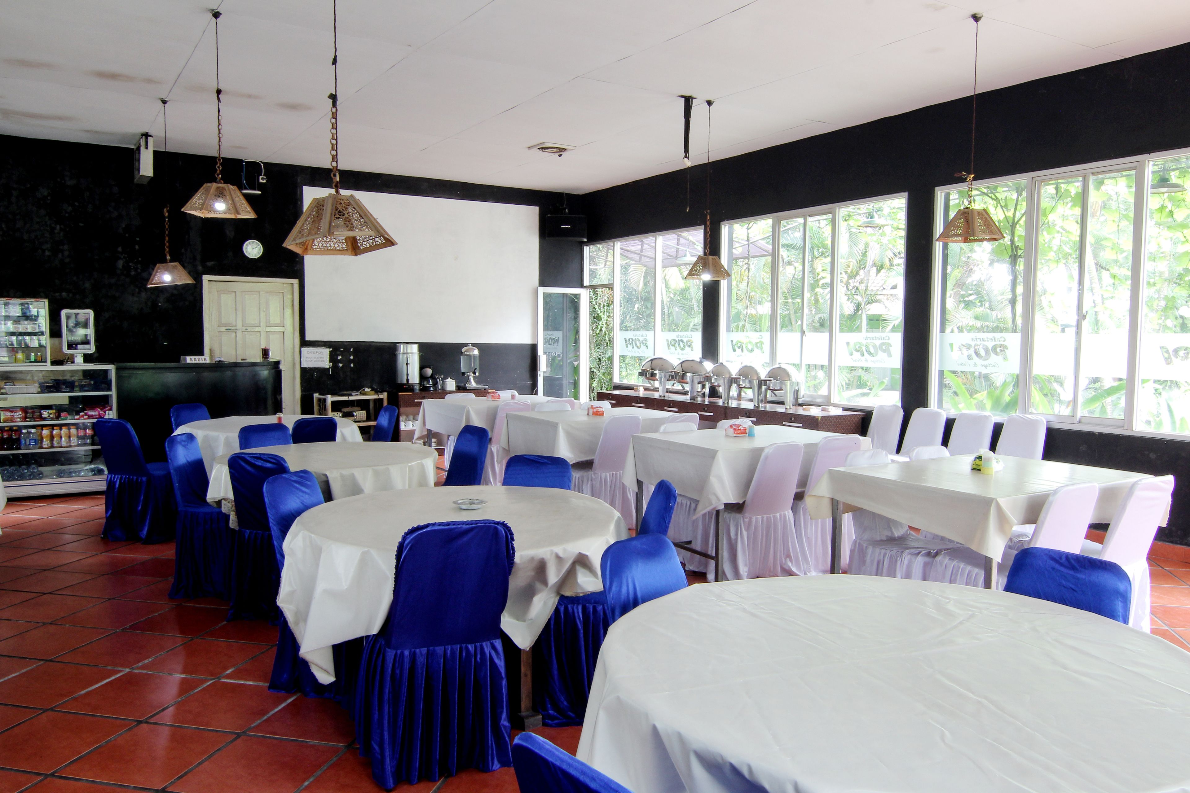 A restaurant with round tables covered in white tablecloths, blue chairs, and hanging pendant lights.