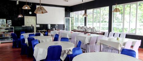 A restaurant with round tables covered in white tablecloths, blue chairs, and hanging pendant lights.