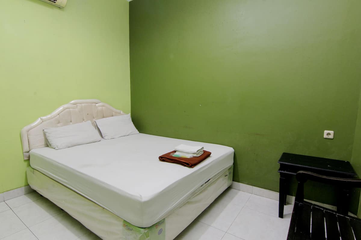 A single-bed room with a green wall, a white mattress, and a small black table.