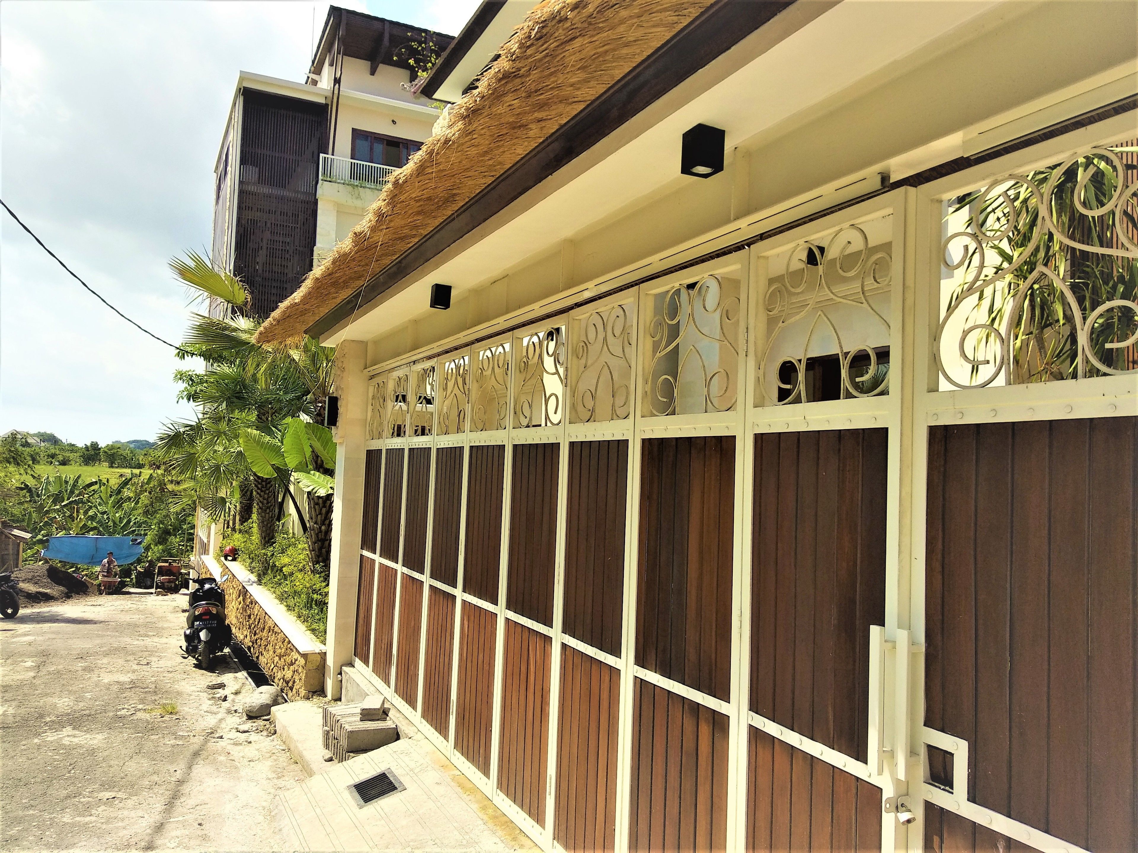 A residential building with a thatched roof, decorative metal gates, and a paved driveway.