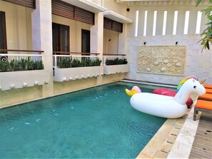 A swimming pool with a unicorn float, a wooden deck, and a wall with a decorative relief. - Rumah Padi Guest House (Tibubeneng)