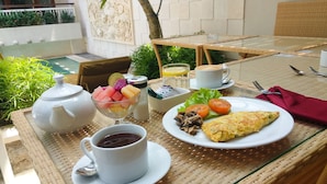 A table set with a teapot, cup, bowl of fruit, plate with vegetables and omelette, and a glass of juice. - Rumah Padi Guest House (Tibubeneng)