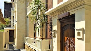 A building with a wooden door, a balcony with a railing, and a palm tree. - Rumah Padi Guest House (Tibubeneng)