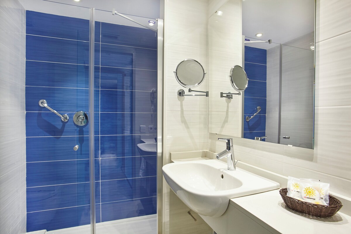 A modern bathroom with a glass-enclosed shower, a white sink, and a large mirror.