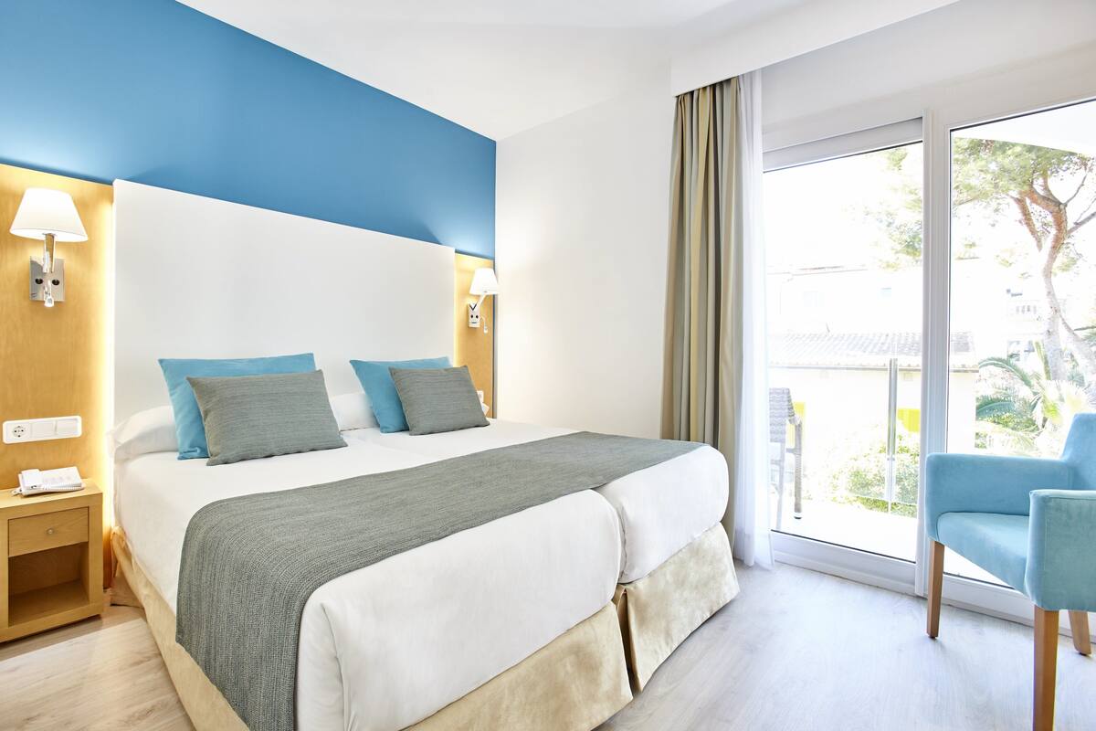 Quarto de hotel com cama, abajures, mesa de cabeceira, uma cadeira e vista para o exterior.