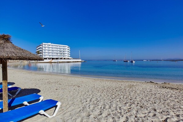 A beach with a hotel, clear blue water, and a few boats. - Universal Casa Marquesa (Ses Salines)