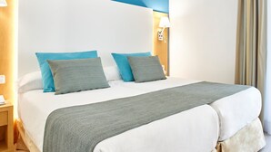 Habitación de hotel con una cama grande, dos almohadas, una mesita de noche, una lámpara y una cortina.