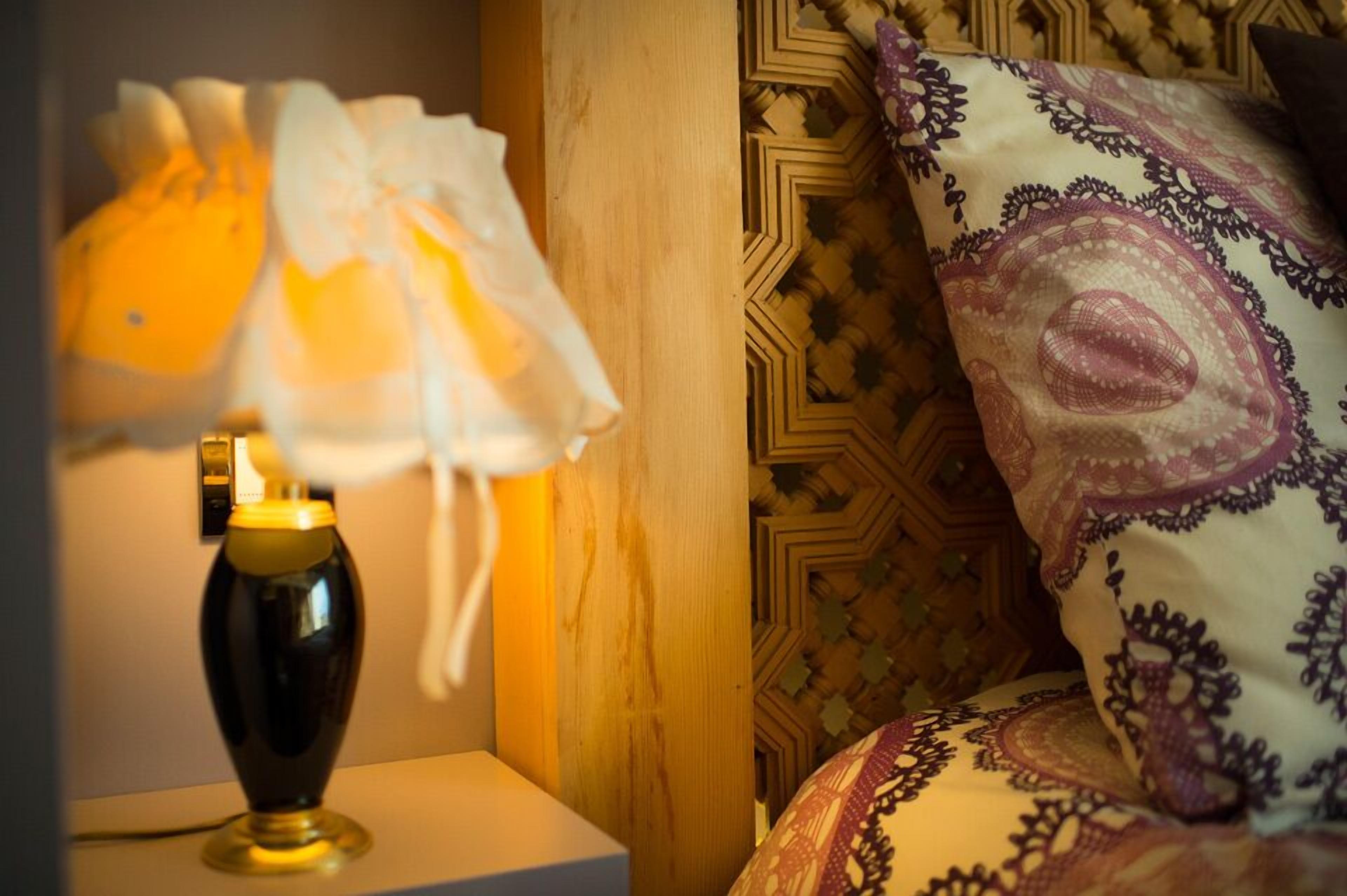 A bedside table with a lamp and a patterned pillow on a bed with a geometric-patterned headboard.
