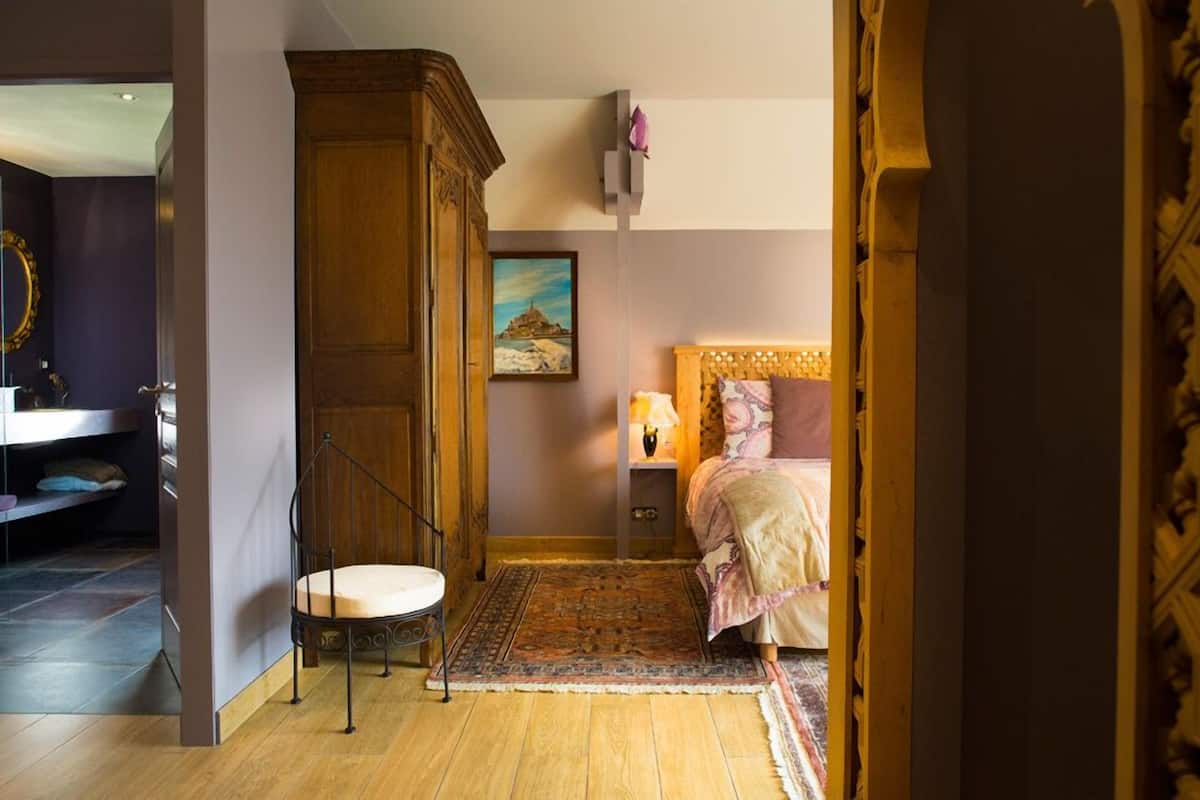 Een slaapkamer met een bed, nachtkastje, lamp, houten kledingkast, stoel en vloerkleed.