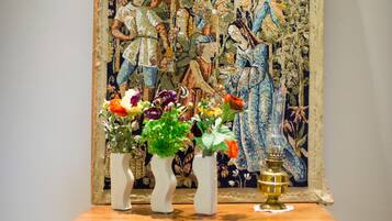 Ein hölzerner Konsolentisch mit drei weißen Vasen, die Blumen enthalten, vor einem Wandteppich mit aufwendigem, farbenfrohem Muster.