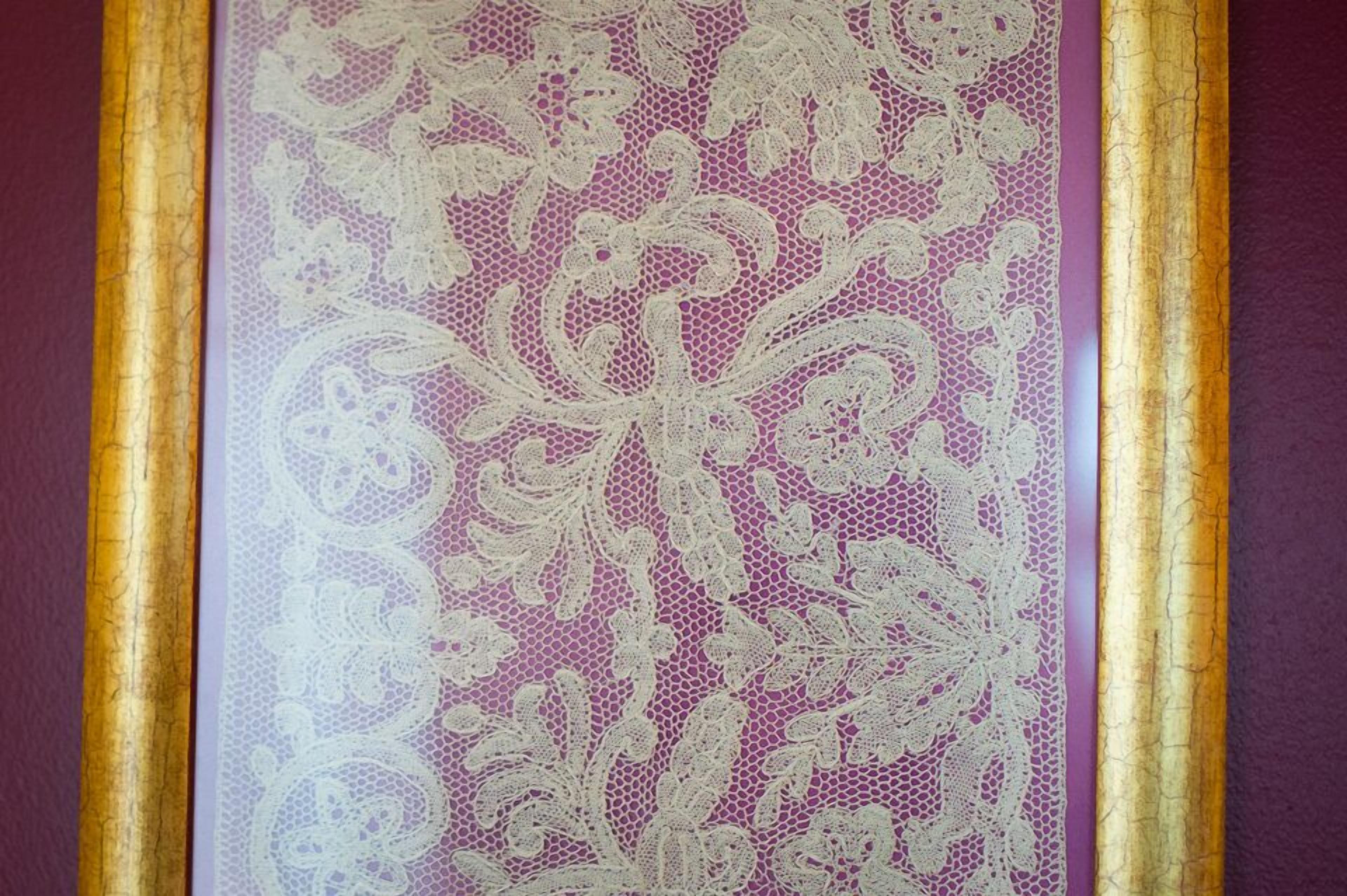 A close-up of a lace curtain with a floral pattern, framed by a gold border.