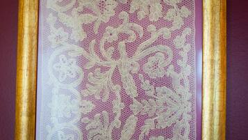 A close-up of a lace curtain with a floral pattern, framed by a gold border.