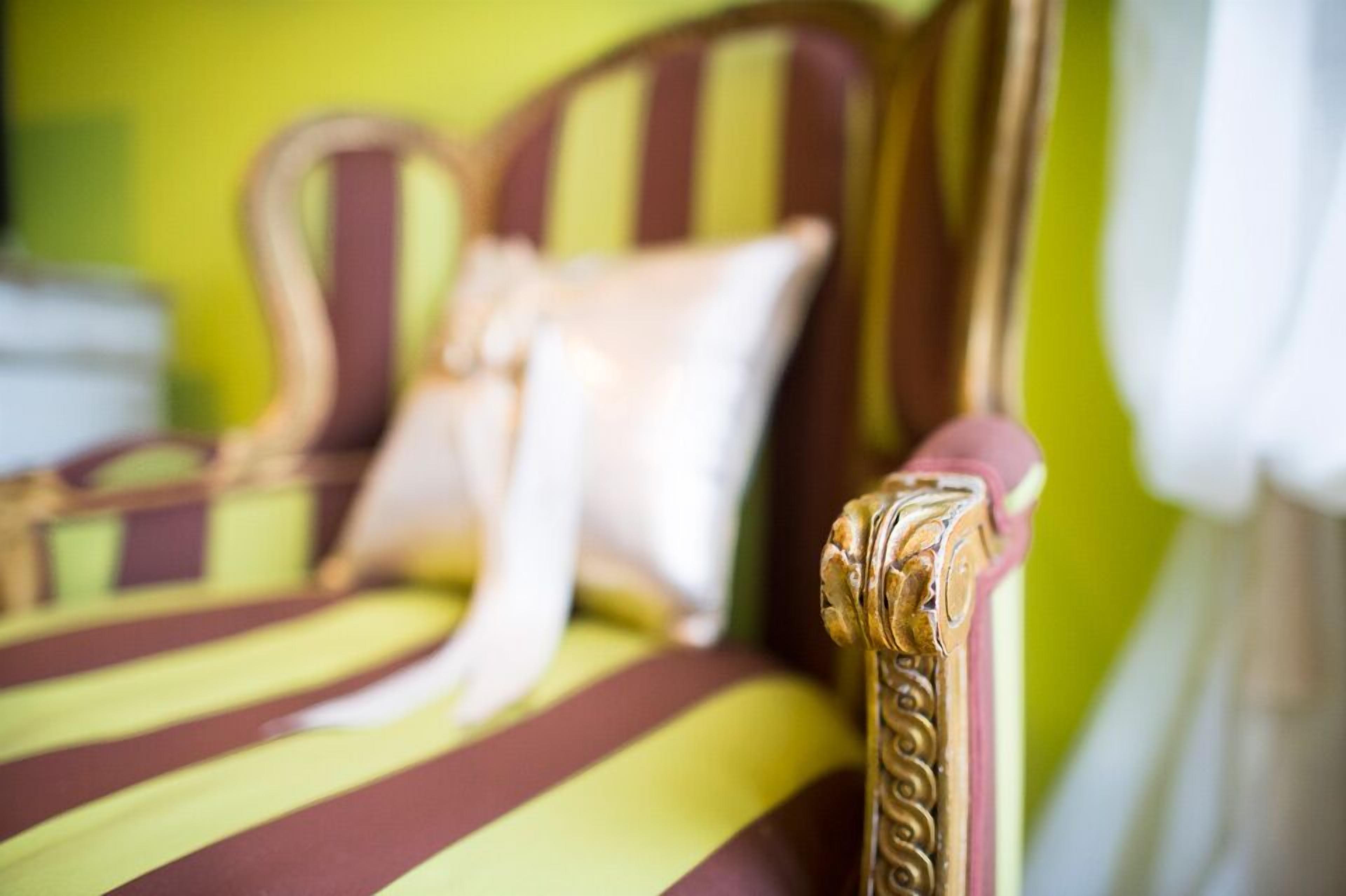 A close-up of a striped sofa with ornate detailing, set against a green wall.