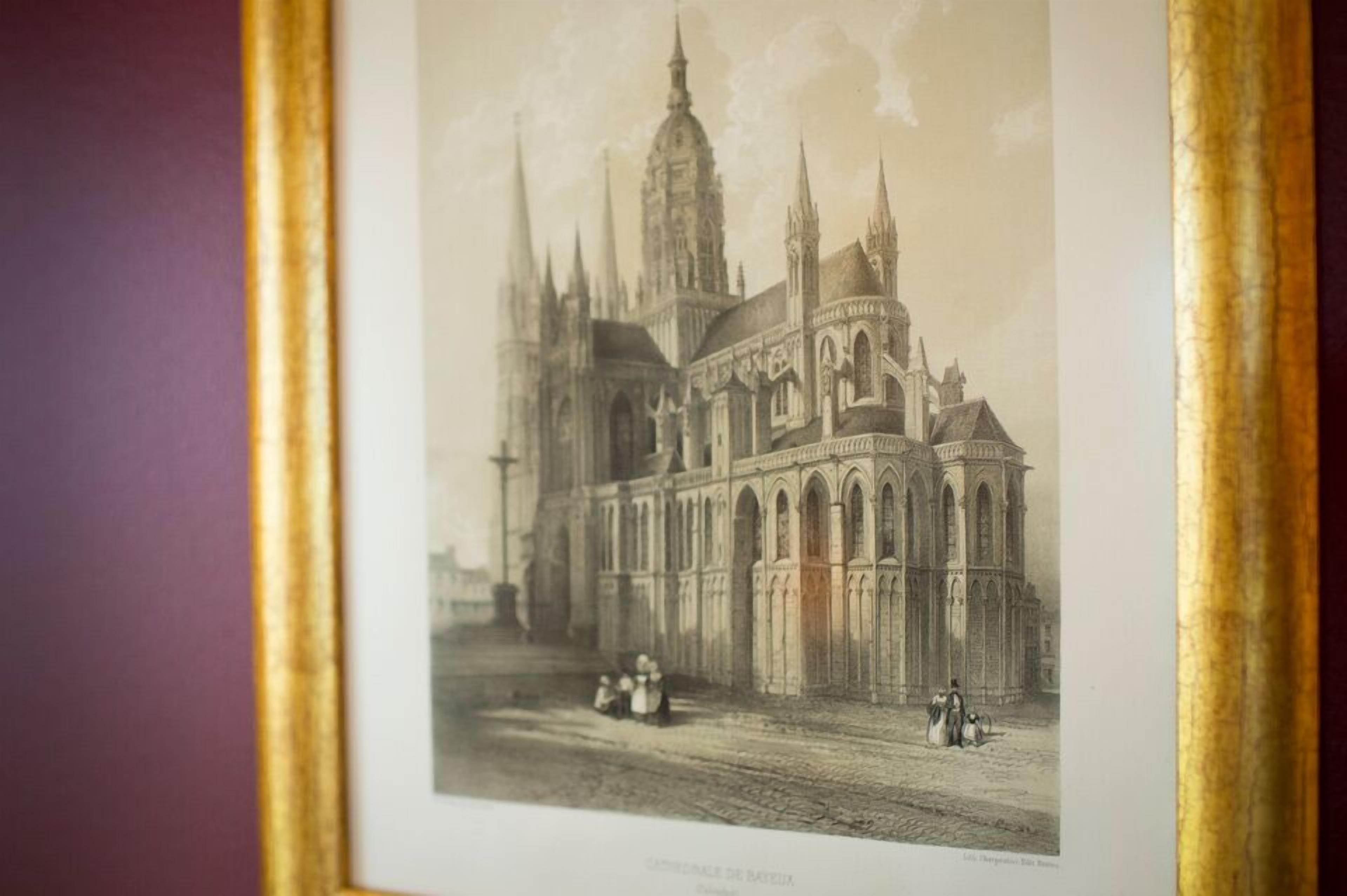 Een lijstfoto van een zwart-wit foto van een gotische kathedraal met een hoge spits, boogvensters en een geplaveid straatje ervoor.