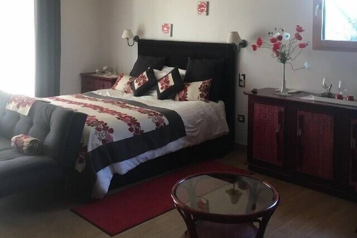 Een slaapkamer met een bed, een glazen tafel, een houten kast en een raam met gordijnen.