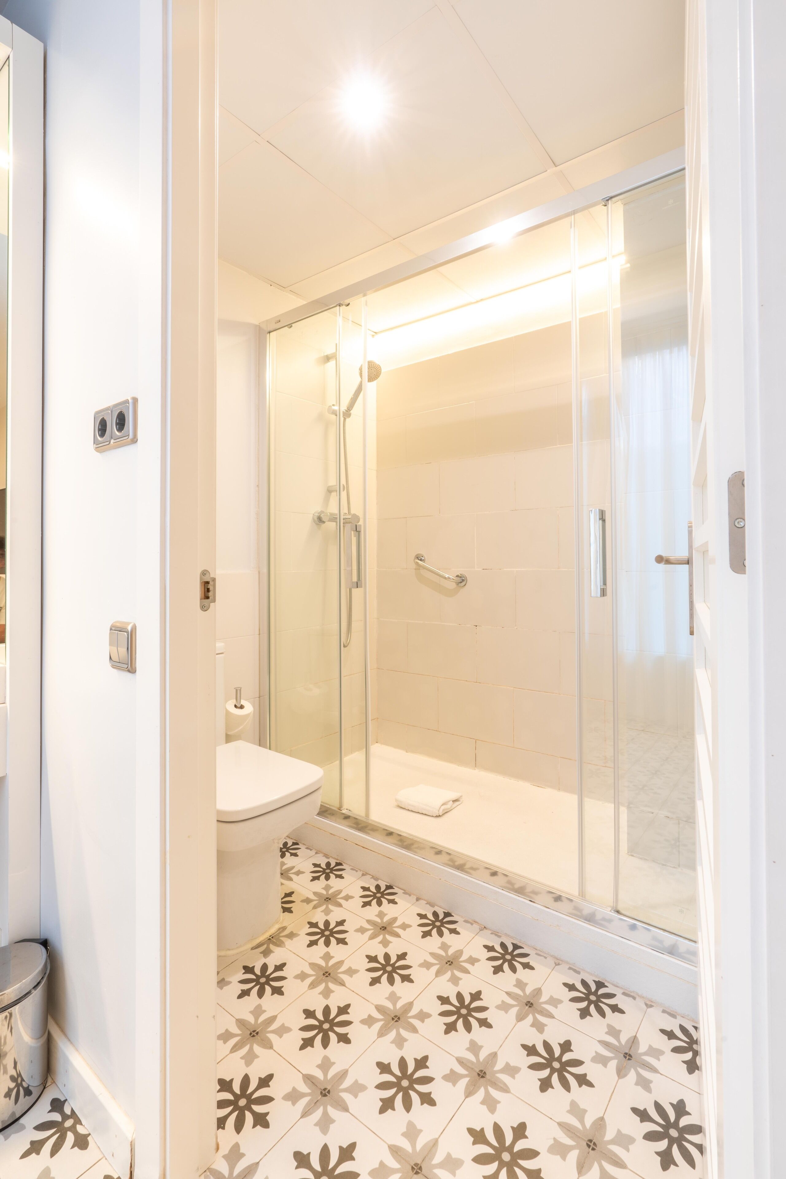 A modern bathroom with a glass-enclosed shower, a toilet, and a patterned floor.