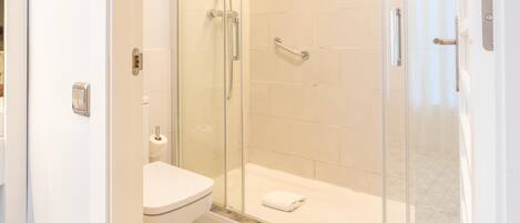 A modern bathroom with a glass-enclosed shower, a toilet, and a patterned floor.