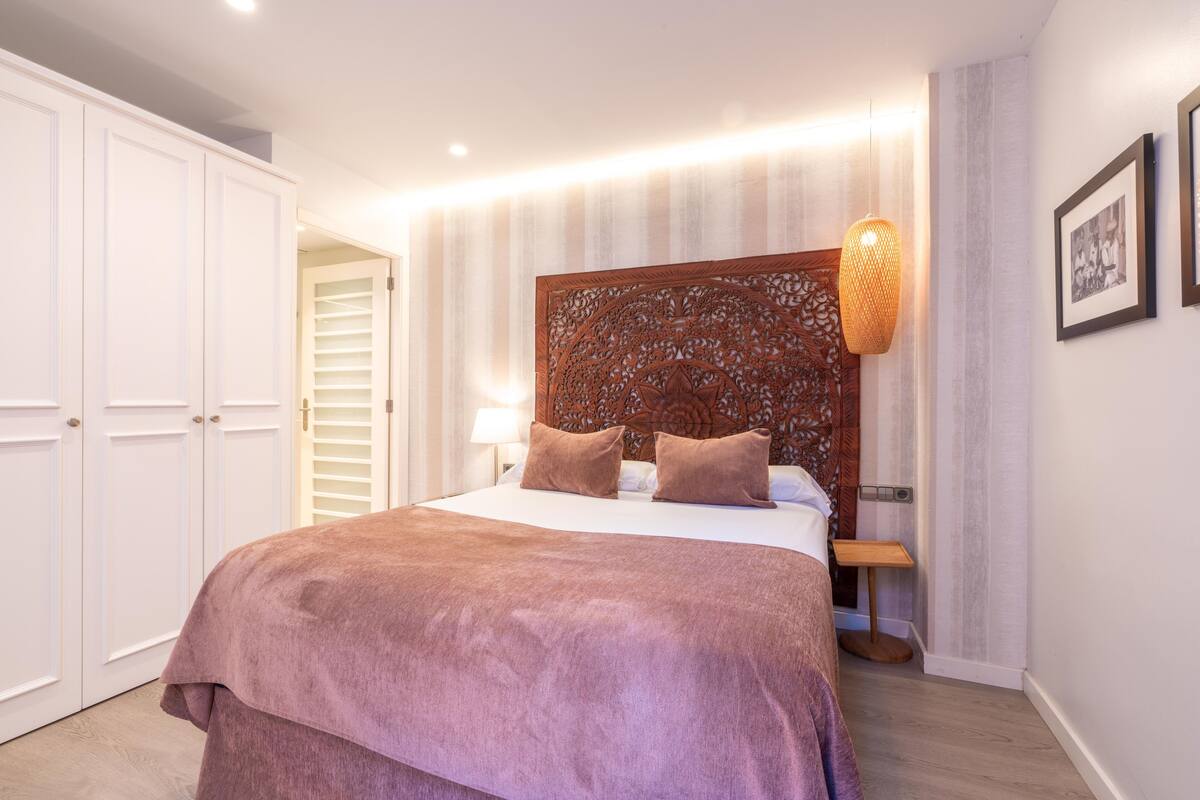 A bedroom with a large bed, a wooden headboard, a bedside table, and a wardrobe.
