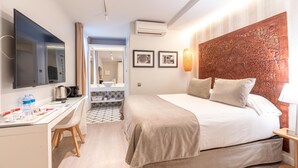 A modern hotel room with a flat-screen TV, a desk with a kettle, a bed with a headboard, and a bathroom visible through an open door. - Serennia Fira Gran Vía Exclusive Rooms (L'Hospitalet de Llobregat)