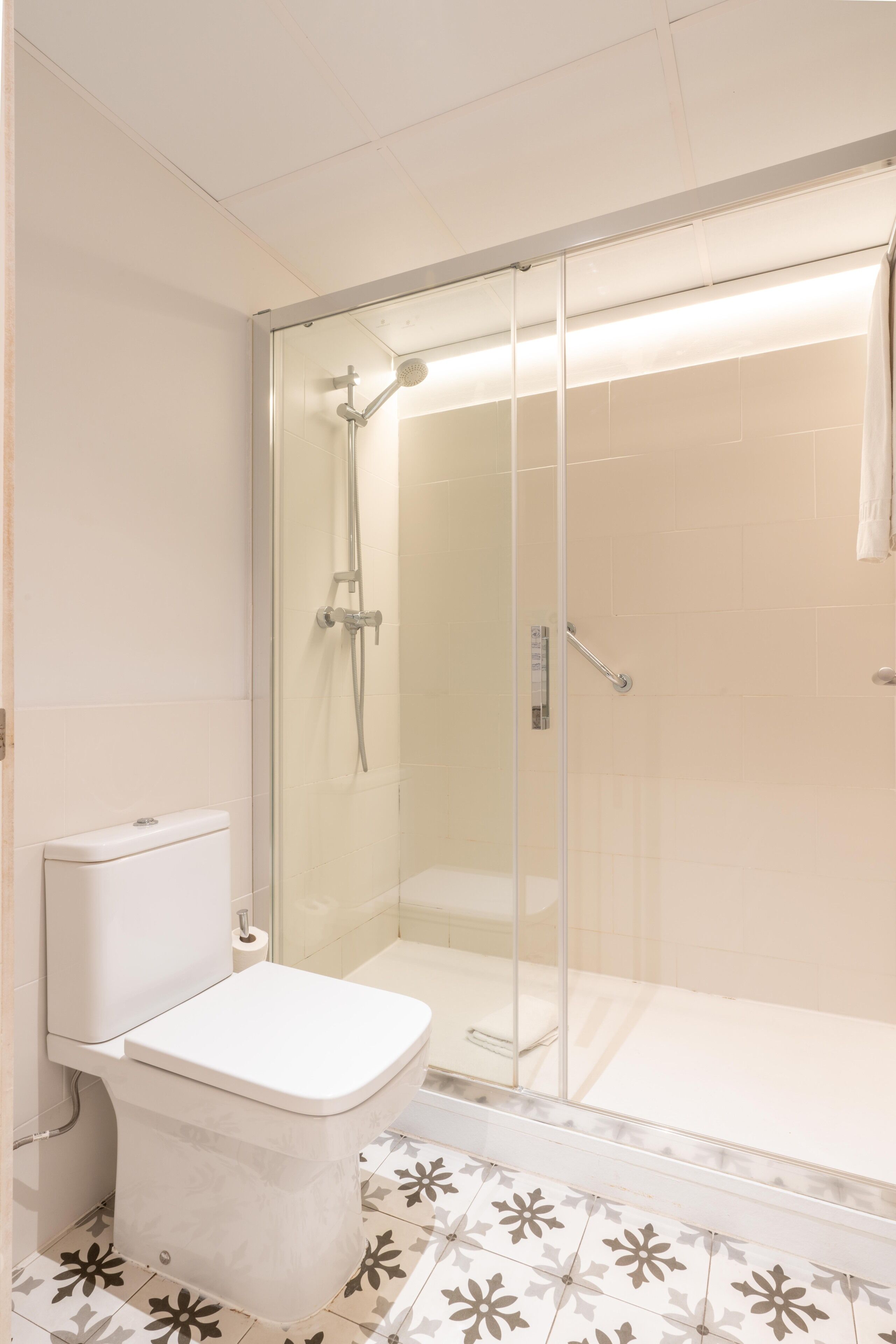Een badkamer met toilet, douchecabine en vloertegels met een patroon.