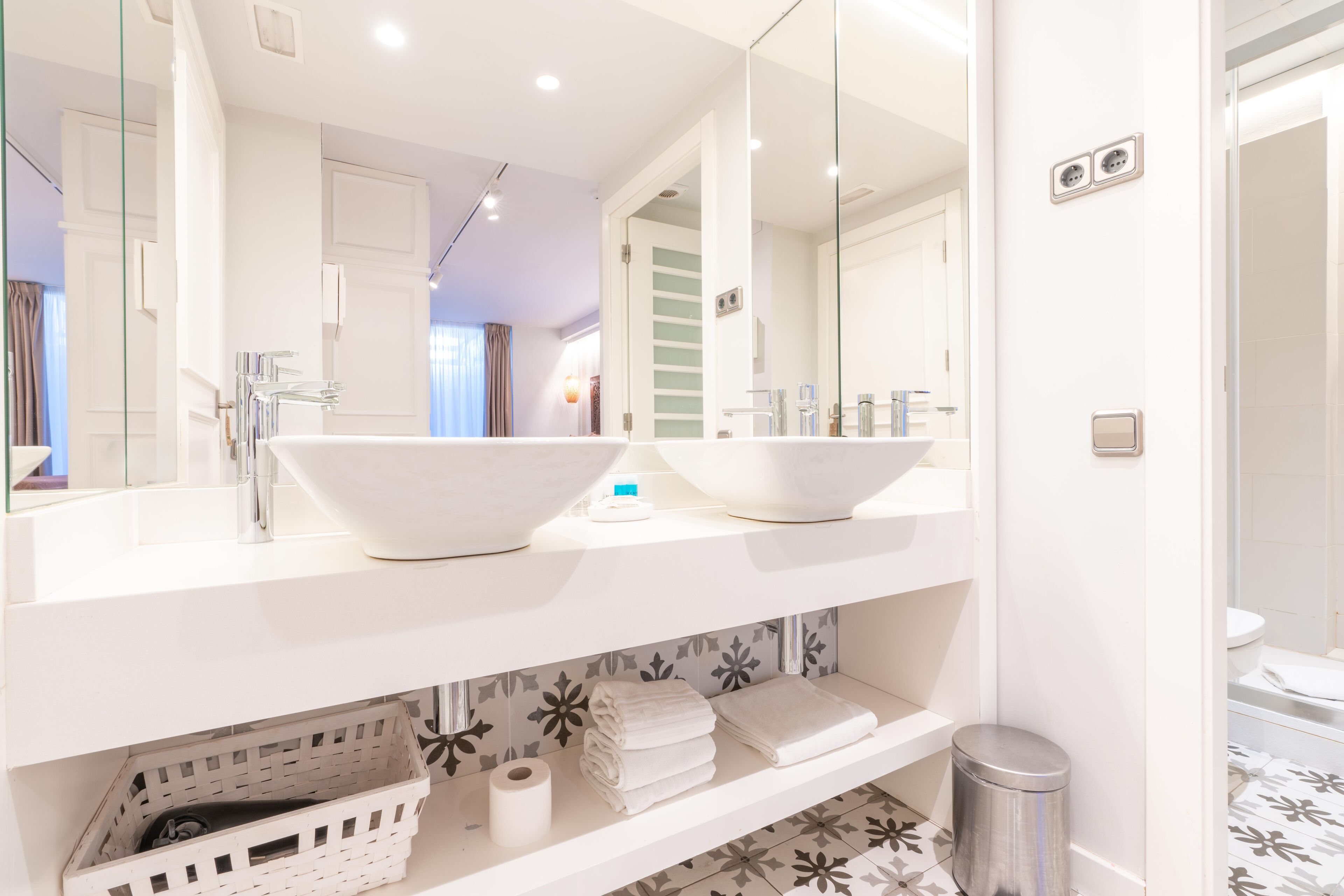 A modern bathroom with two large white sinks, a mirror, and a white vanity with a basket and towels.