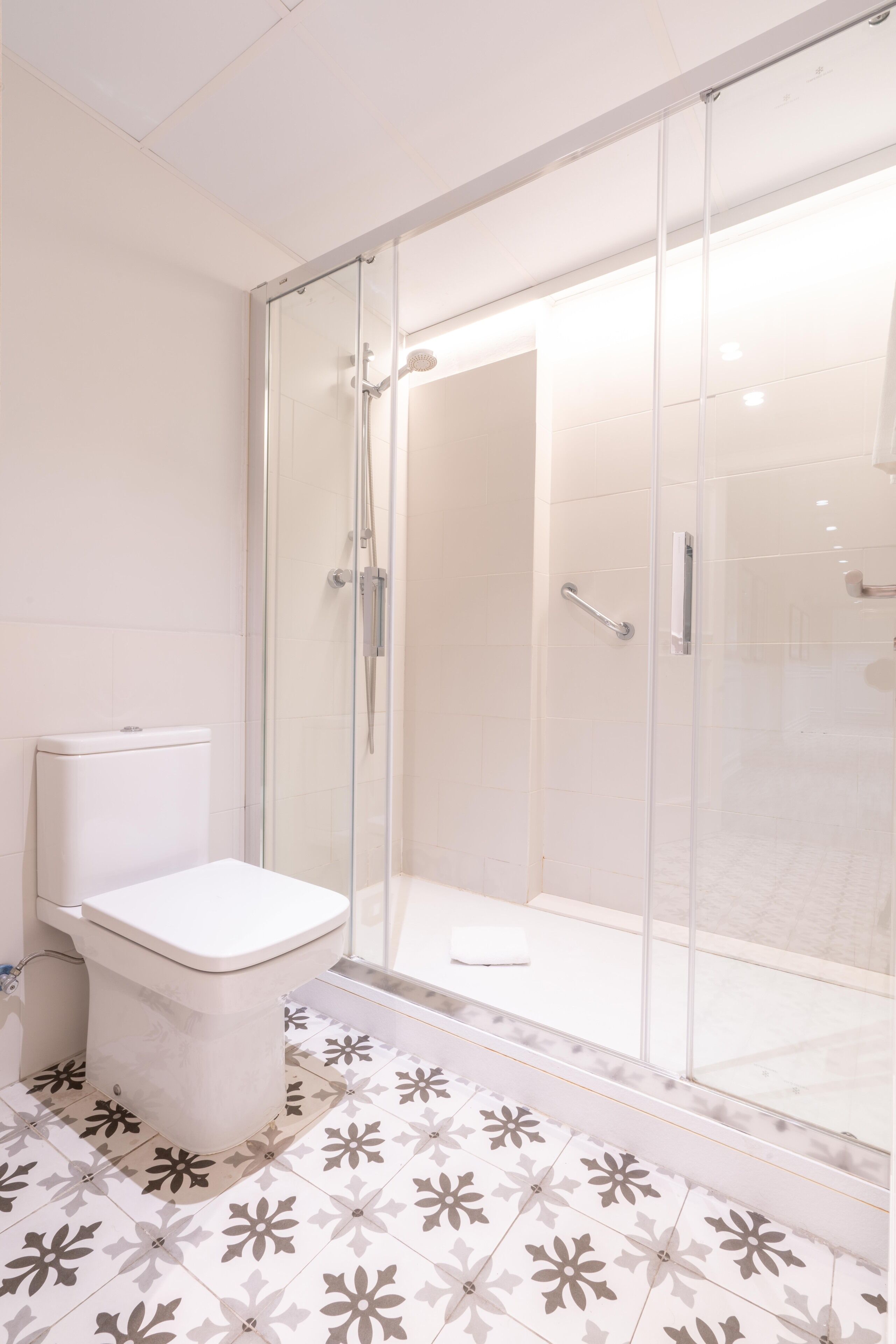 A modern bathroom with a glass-enclosed shower, a toilet, and patterned floor tiles.